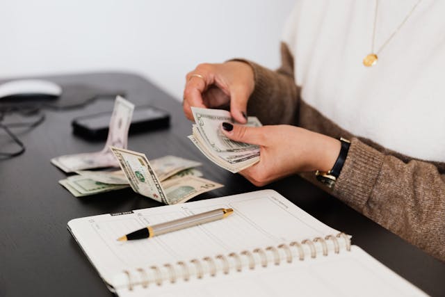 Person counting money with a pen and notepad in front of them
