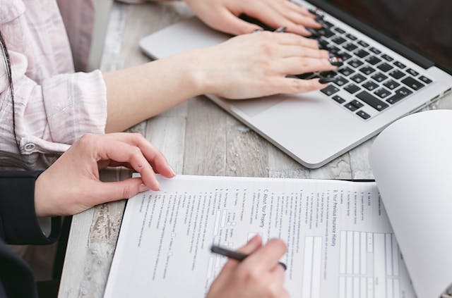 Person typing on a laptop while another person fills out a document