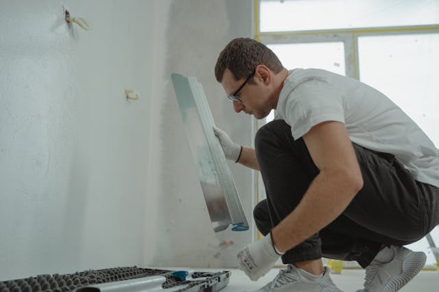 Person wearing glasses and gloves while crouching down surronded by painting supplies
