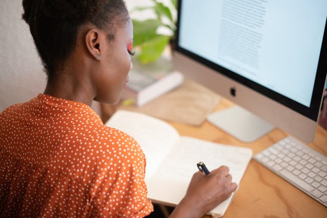 Person looking at a computer and writing in a notebook