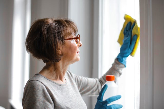 Person wearing glasses and rubber gloves while using a cloth to clean a window