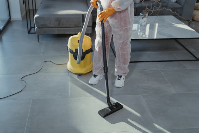 A person in a tyveck suit and yellow gloves, steam cleaning a floor