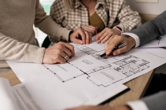 Three people with their hands on a paper showing the blueprint of a home