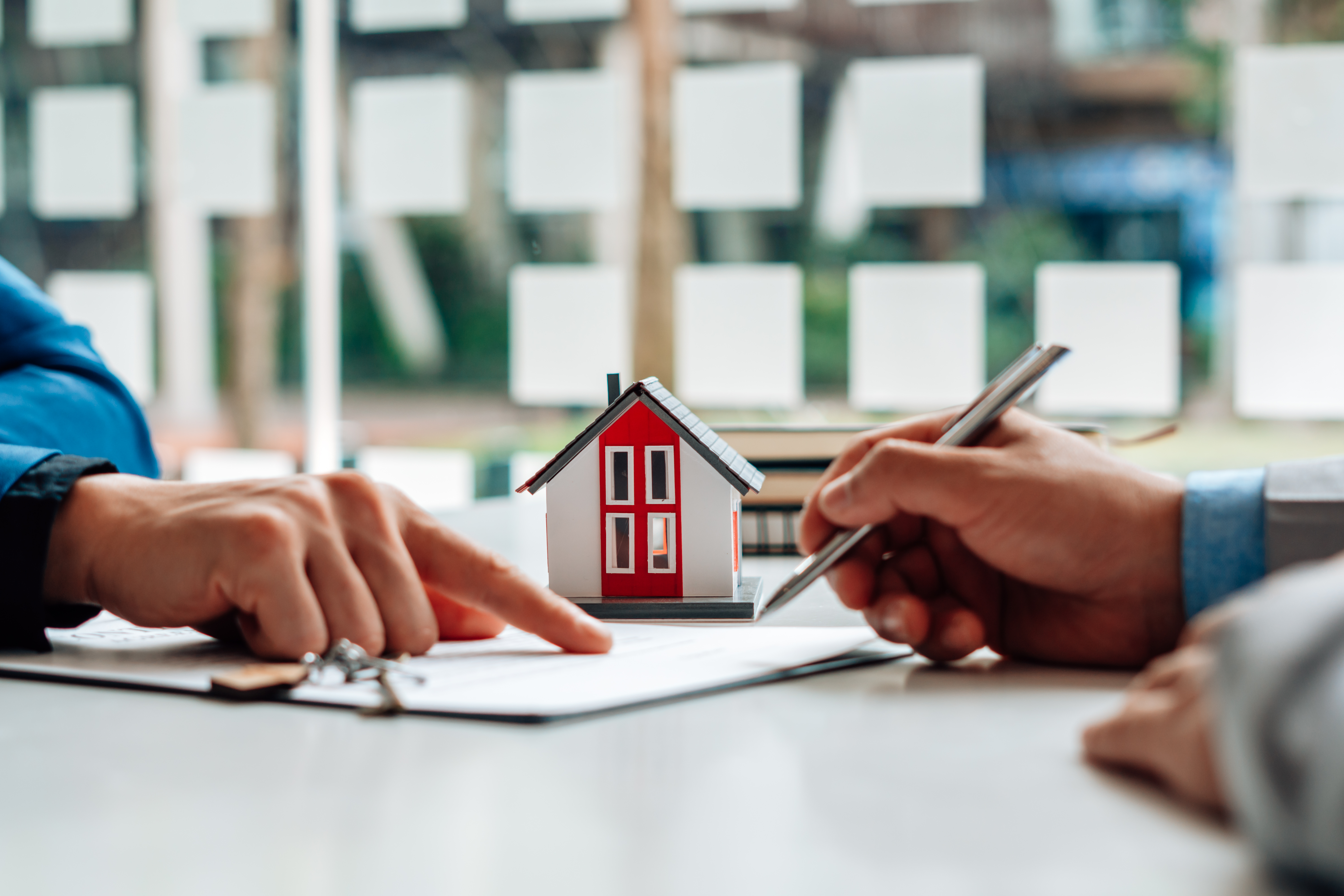 hands-reviewing-documents-with-small-house-model-on-desk