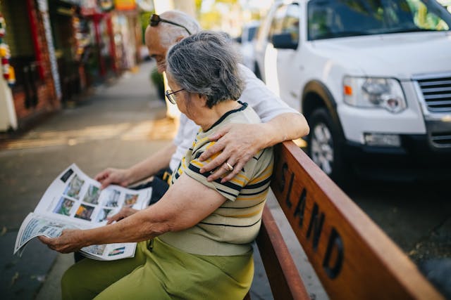 Two people sitting on a bench reading a newspaper
