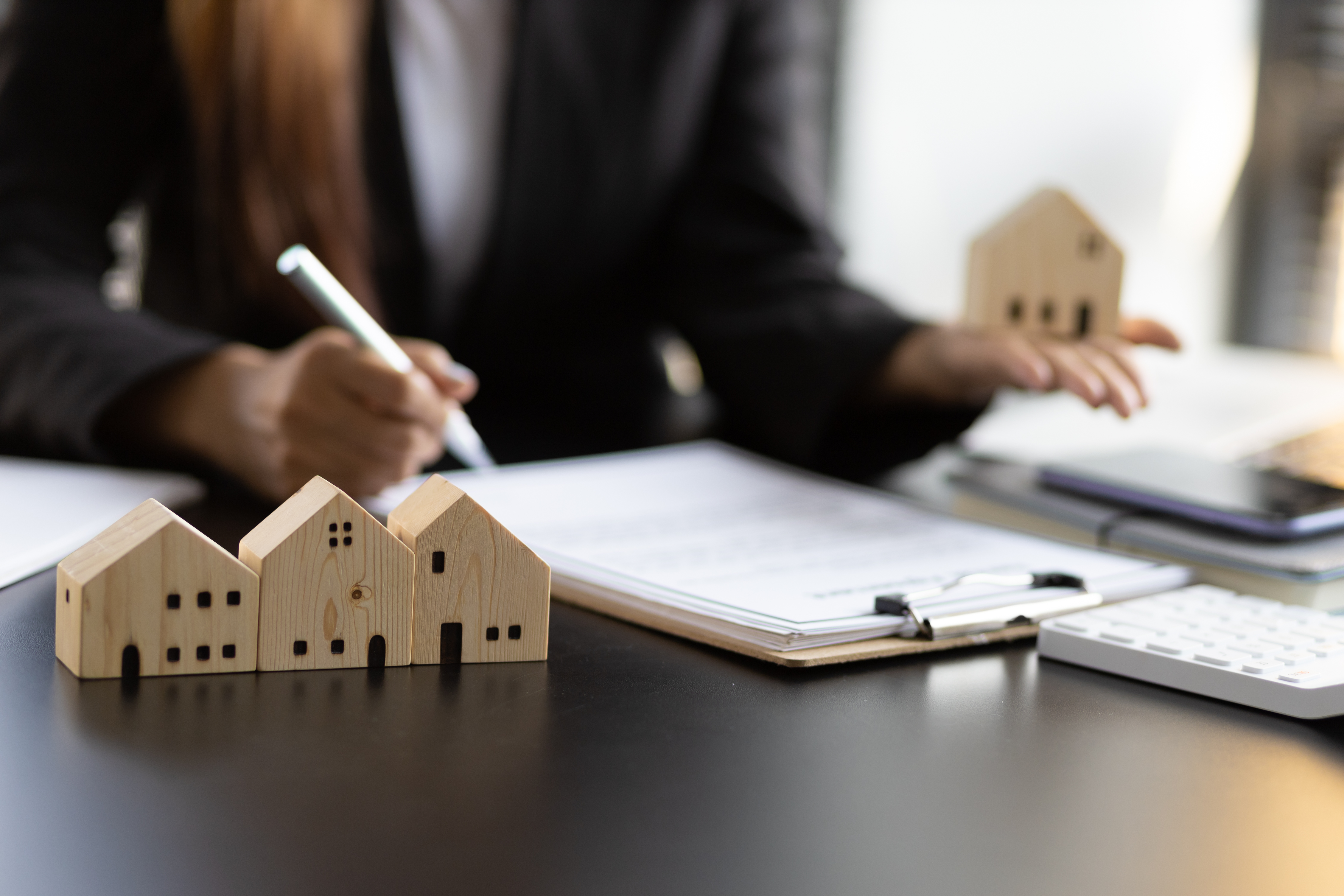 person-writing-on-clipboard-with-small-wooden-houses-on-table