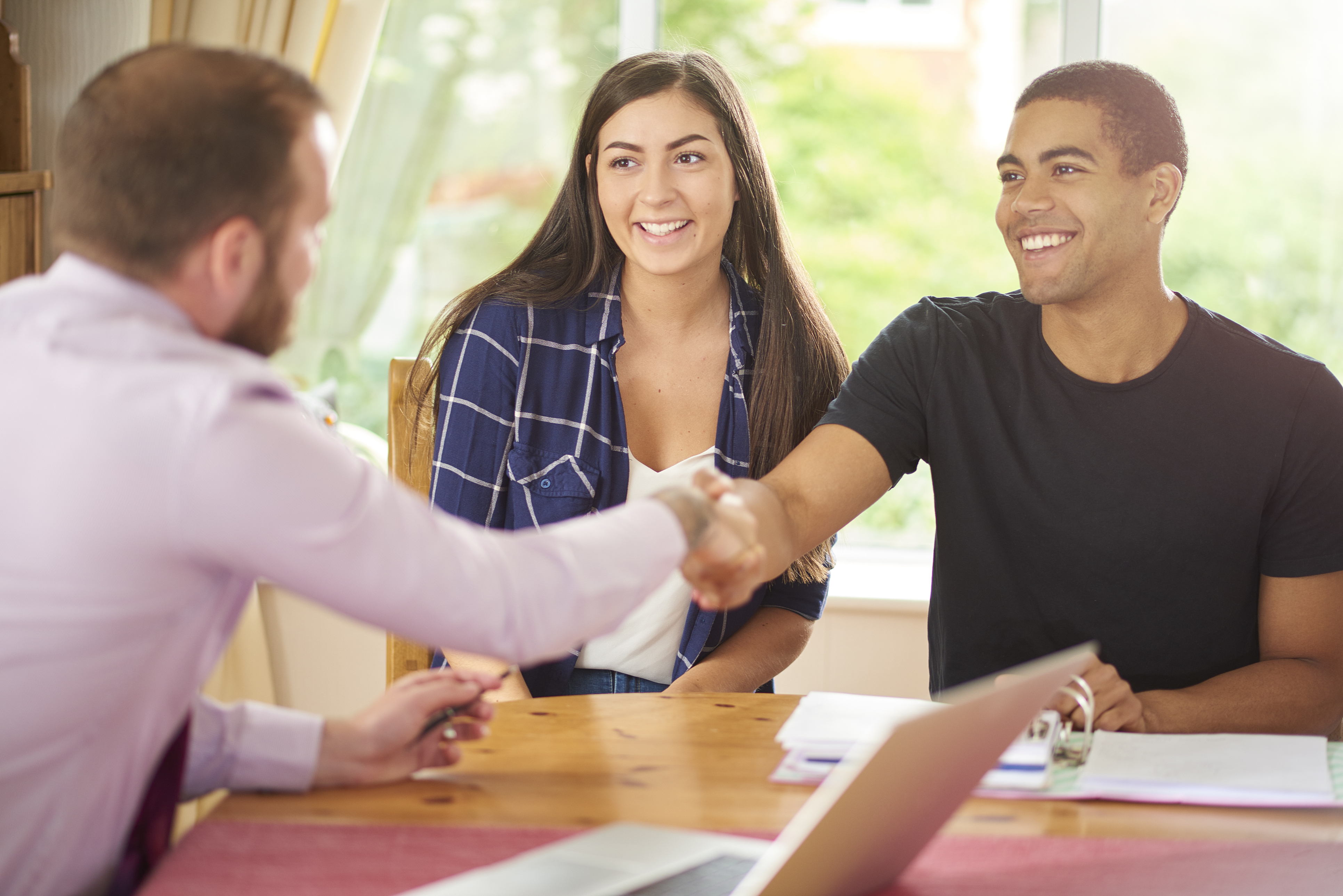 two-people-sitting-across-someone-shaking-hands