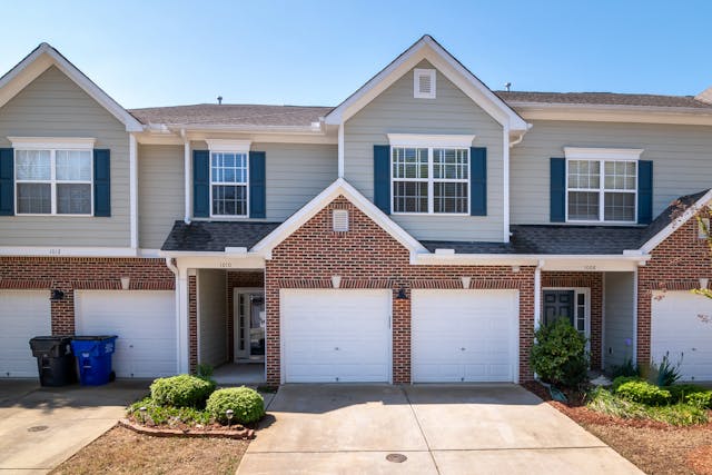 A row of townhomes with brick and siding exteriors, blue window shutters, and attached garages